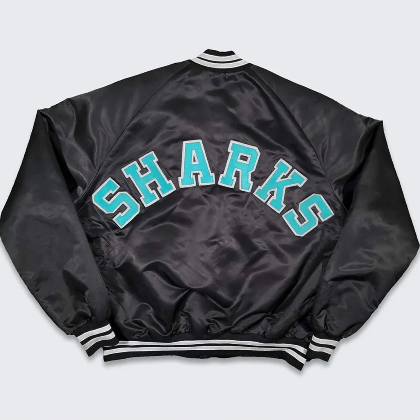 Back of NHL San Jose Sharks satin varsity jacket in black colour featuring large team logo and striped ribbed hem